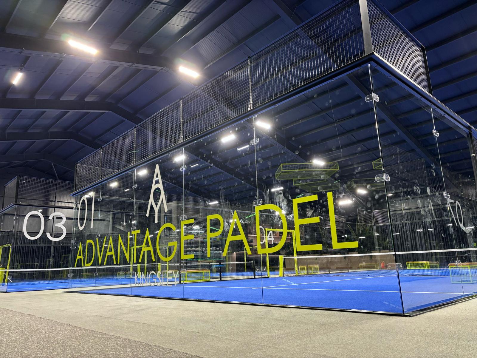 The Advantage Padel Kingsley venue: glass-walled panoramic courts with blue surfaces under indoor lighting